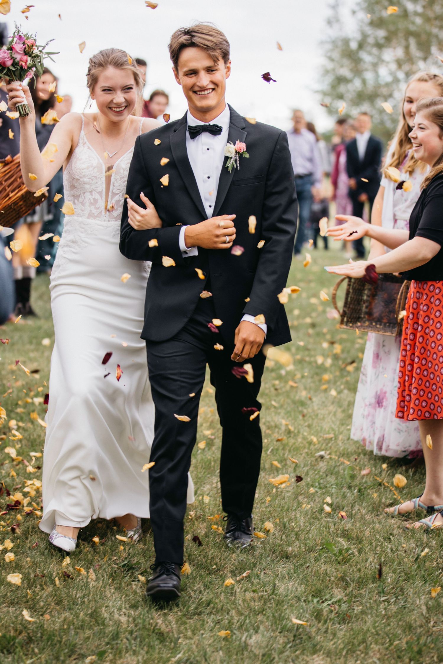 Wedding guests shower newlyweds with confetti during outdoor celebration on grassy lawn.