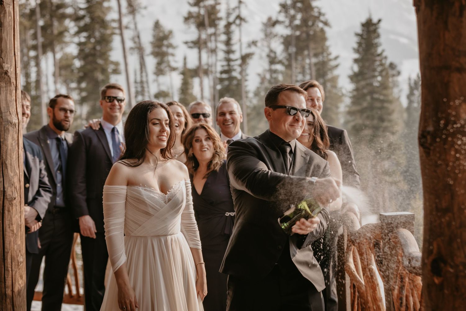 Outdoor winter wedding ceremony with guests gathered among tall pine trees.