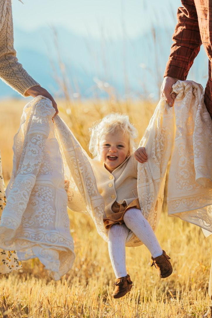 Dancing feet in white lace dresses and brown boots against golden wheat field at sunset.