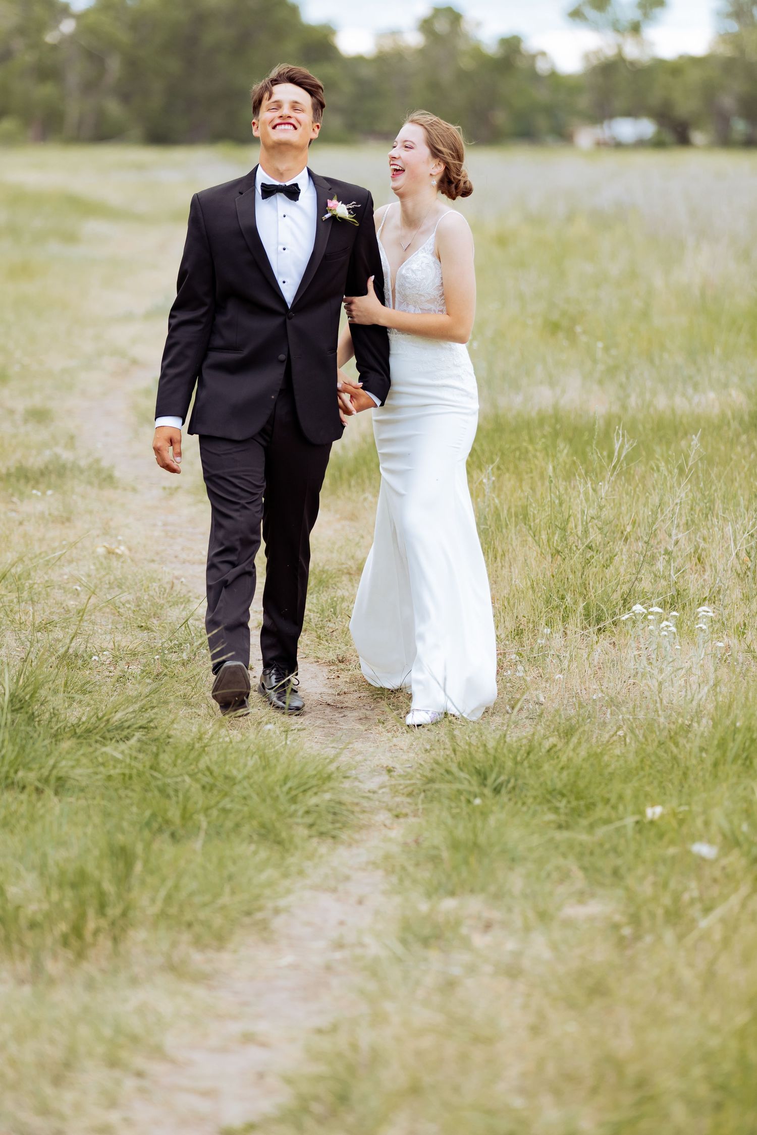 Newlyweds laugh and walk together through a sunny meadow.