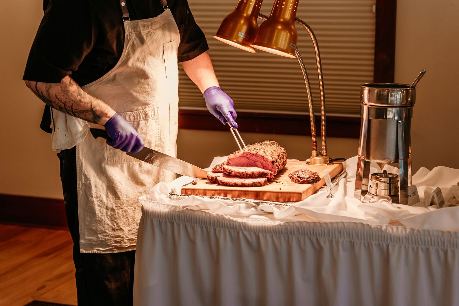 Professional caterer preparing meat dishes at elegant buffet station.