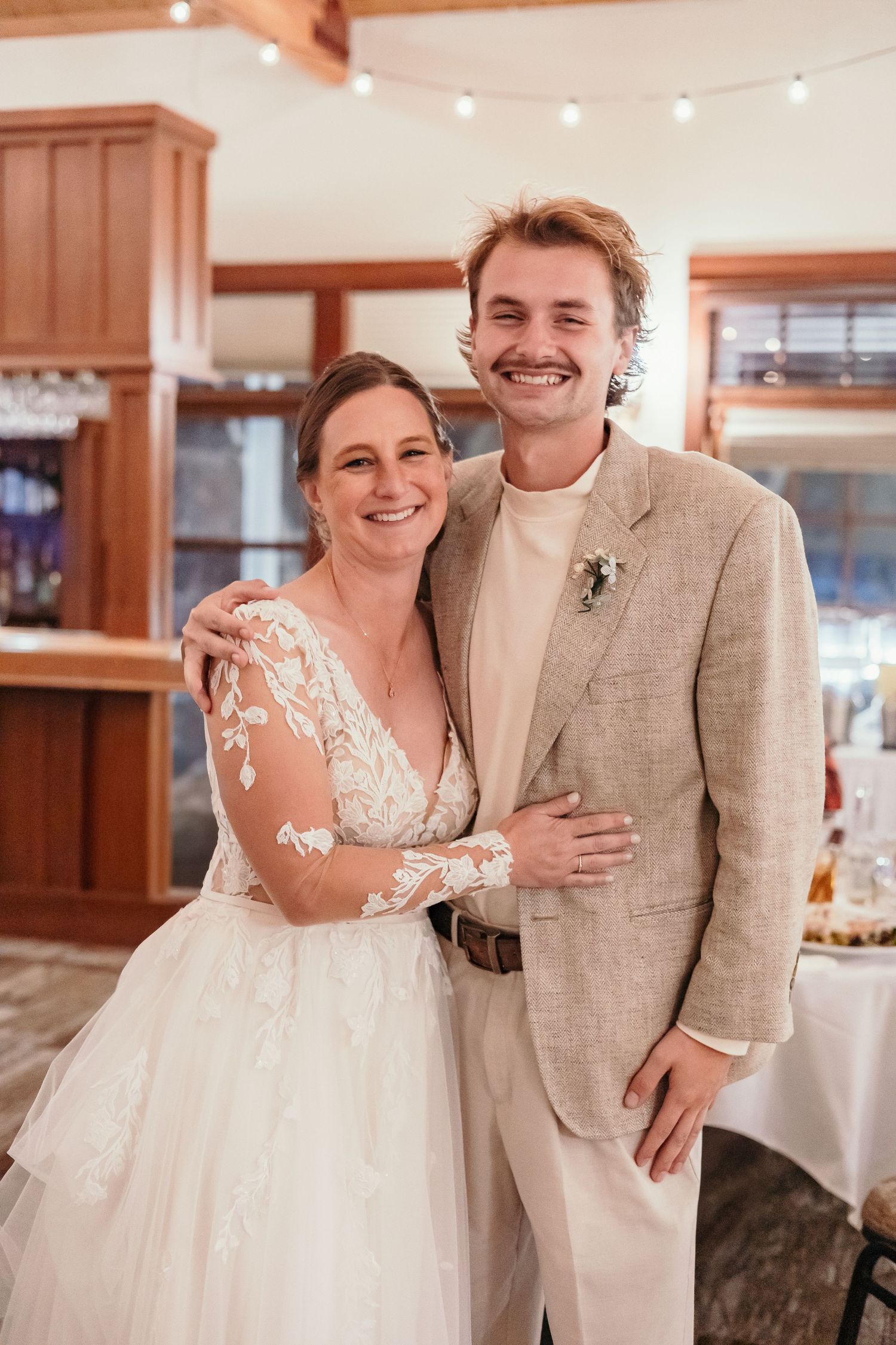 Indoor wedding reception moments with elegant white dress and beige suit.