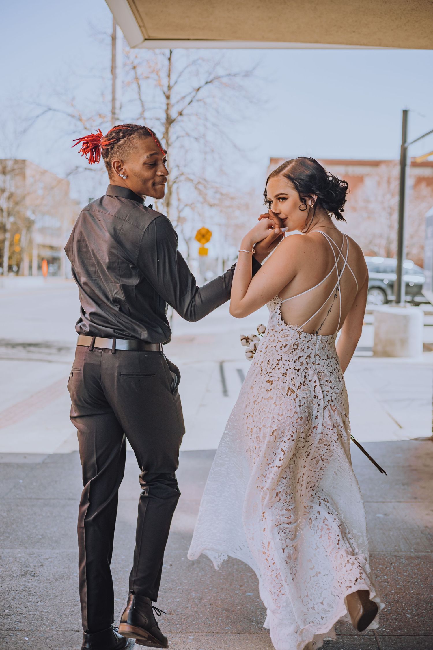 Wedding couple dances playfully in an urban setting with lace dress details.