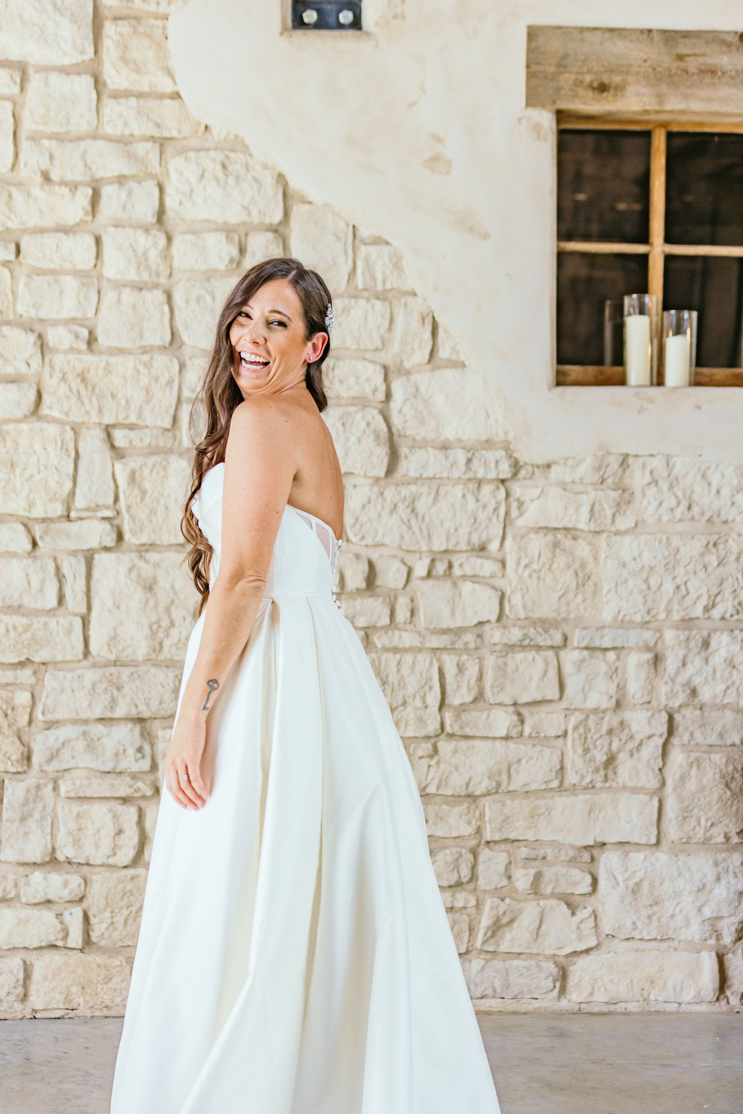 Elegant white wedding dress flowing against stone wall backdrop.