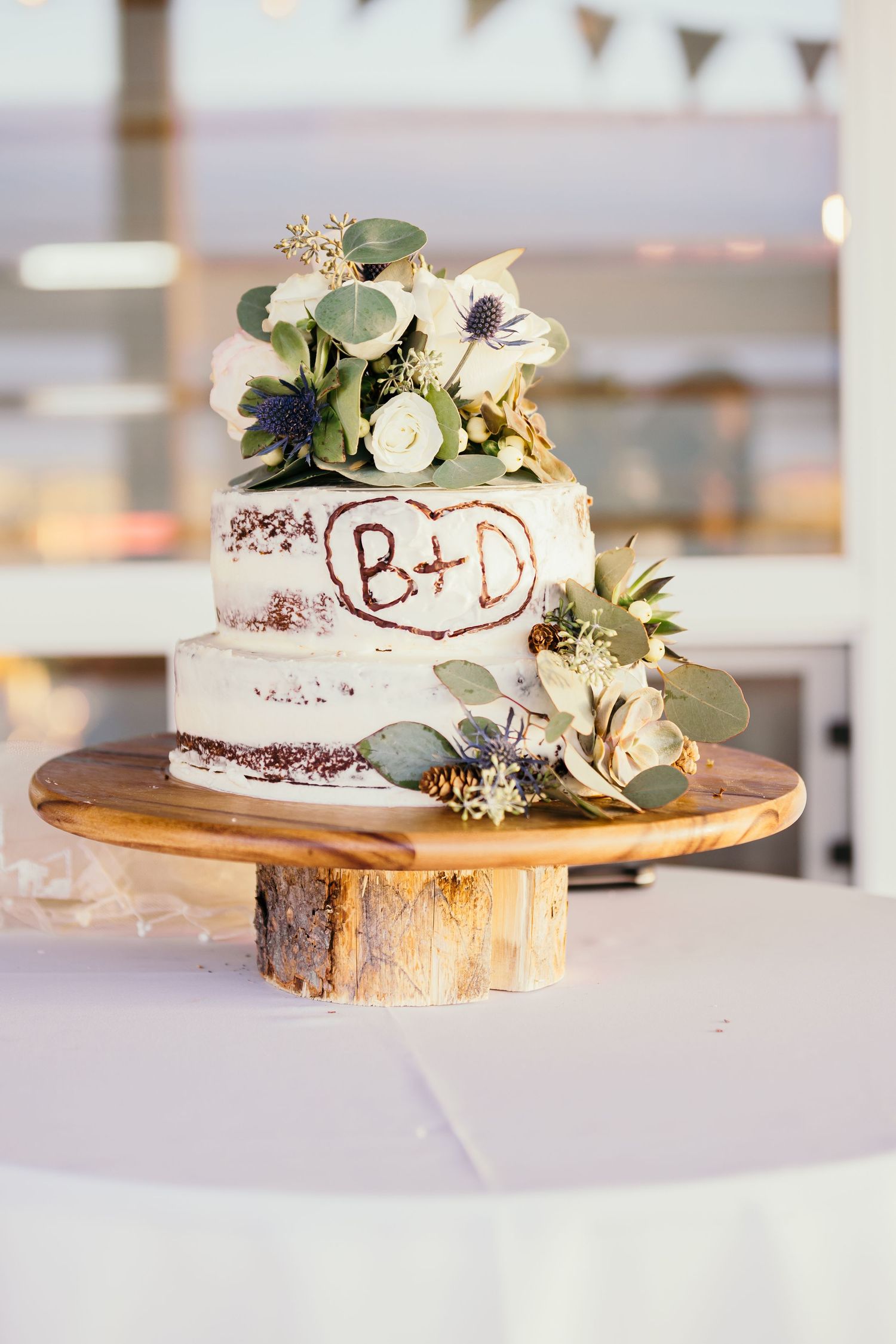 White wedding cake decorated with fresh flowers displayed on rustic wood slice cake stands.