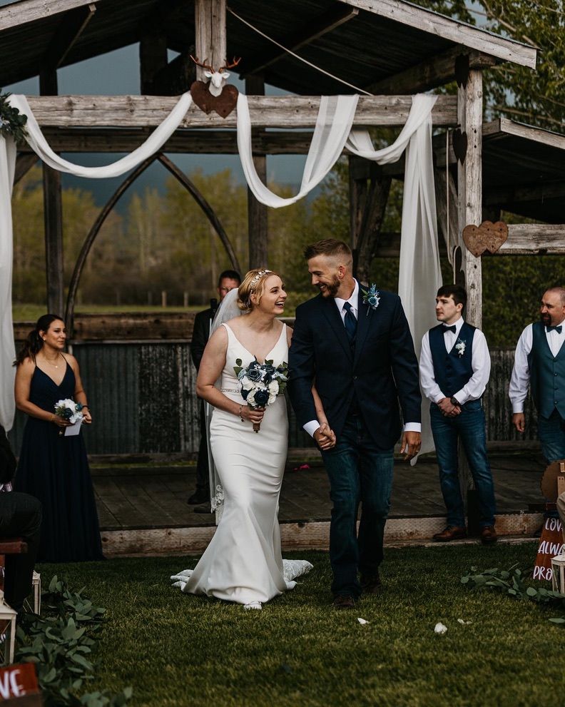 A wedding ceremony under a rustic wooden arch decorated with white fabric draping.