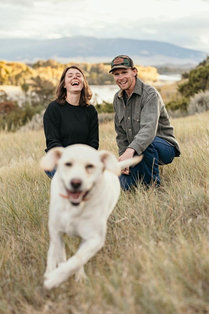 Happy white dog running and playing in tall grass field with mountains in background.