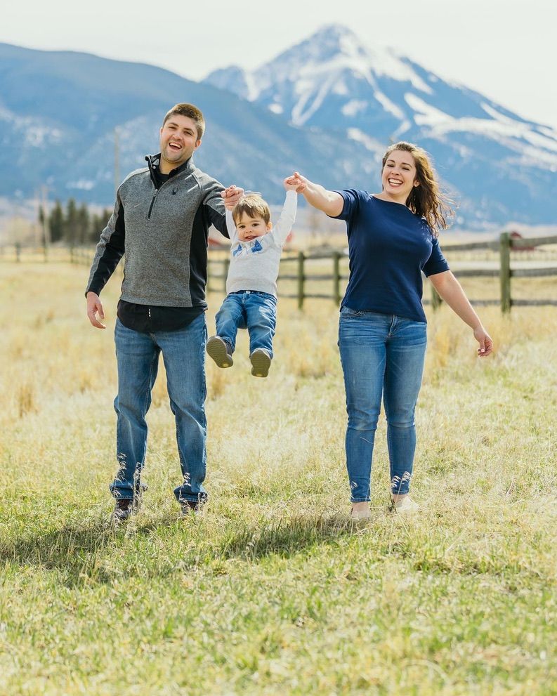 Family playing and jumping together in field with snow-capped mountain in background.