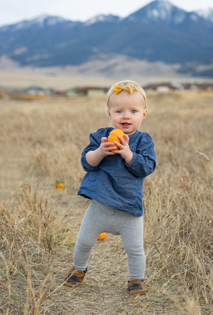 Small child playing with orange toy in tall grass with mountains in background.