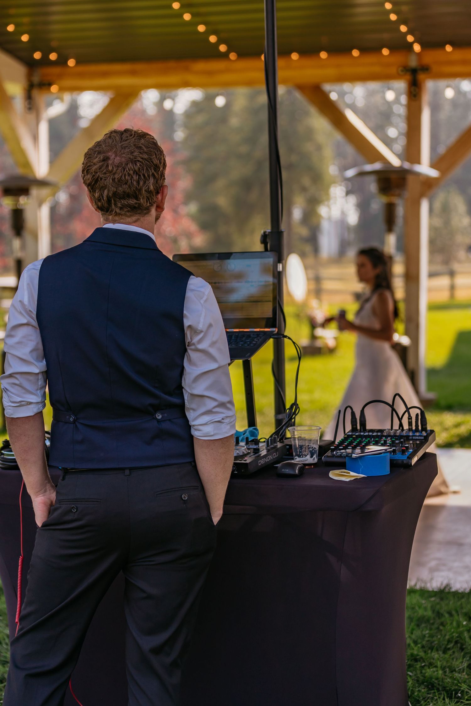 Bar staff in navy vests serving drinks at an outdoor wedding reception under string lights.