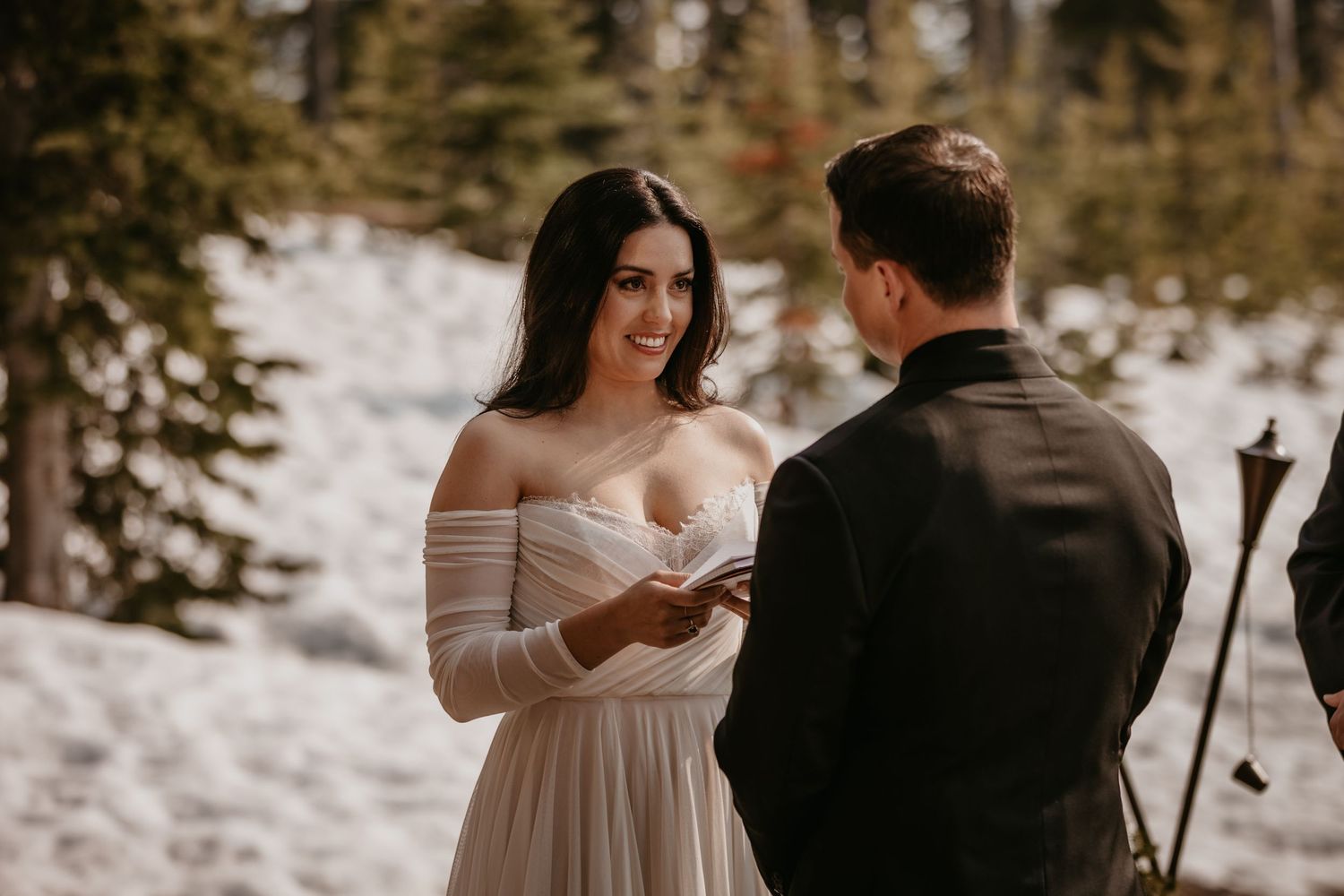 A couple exchanges vows during an intimate outdoor winter ceremony surrounded by snow-covered pine trees.