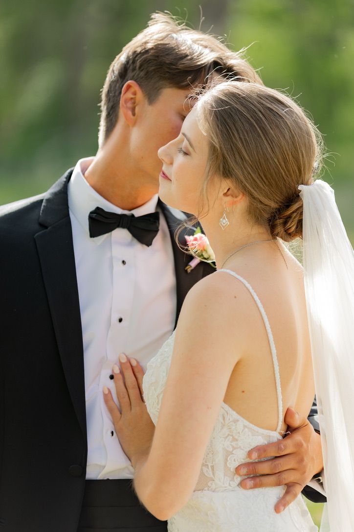 Romantic wedding couple embraces outdoors in formal attire with soft natural lighting.