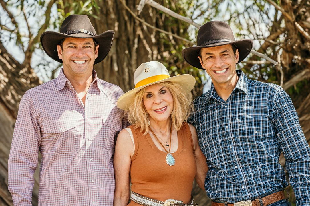 Group portrait in western attire standing among trees on a sunny day.