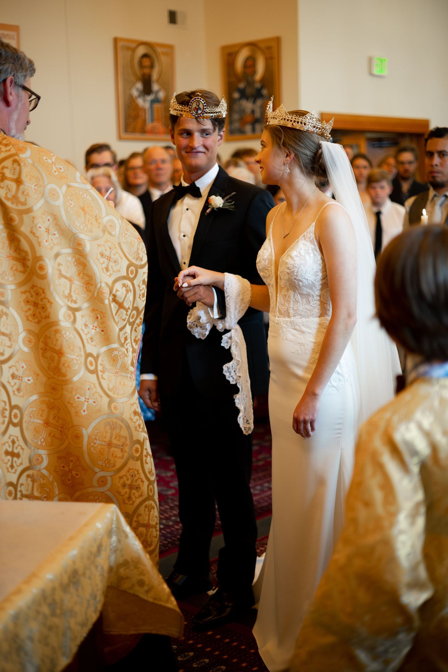 Traditional Orthodox Christian wedding ceremony with couple and priest in ornate gold vestments inside church sanctuary.