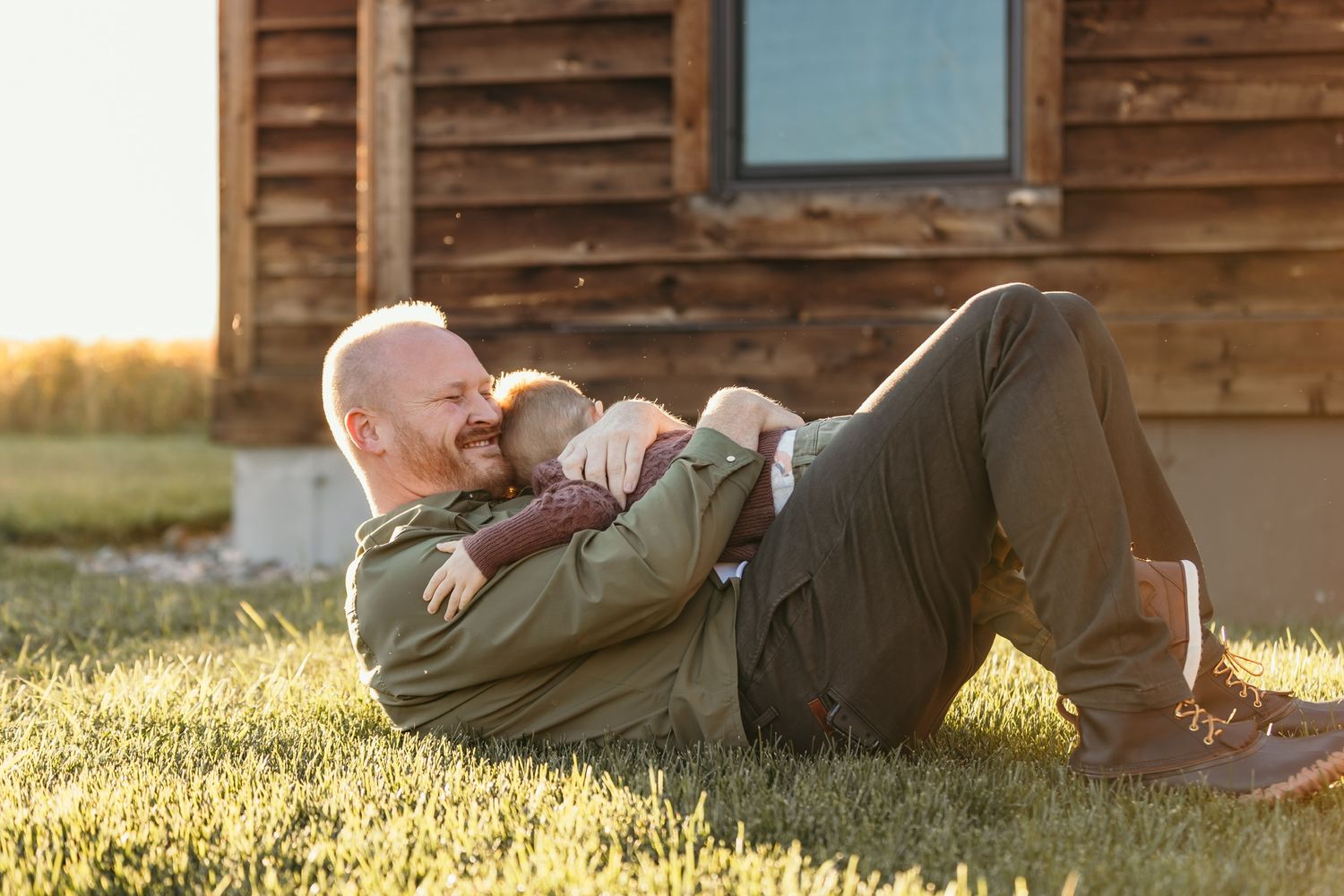 People relaxing on grass near wooden building during sunset.