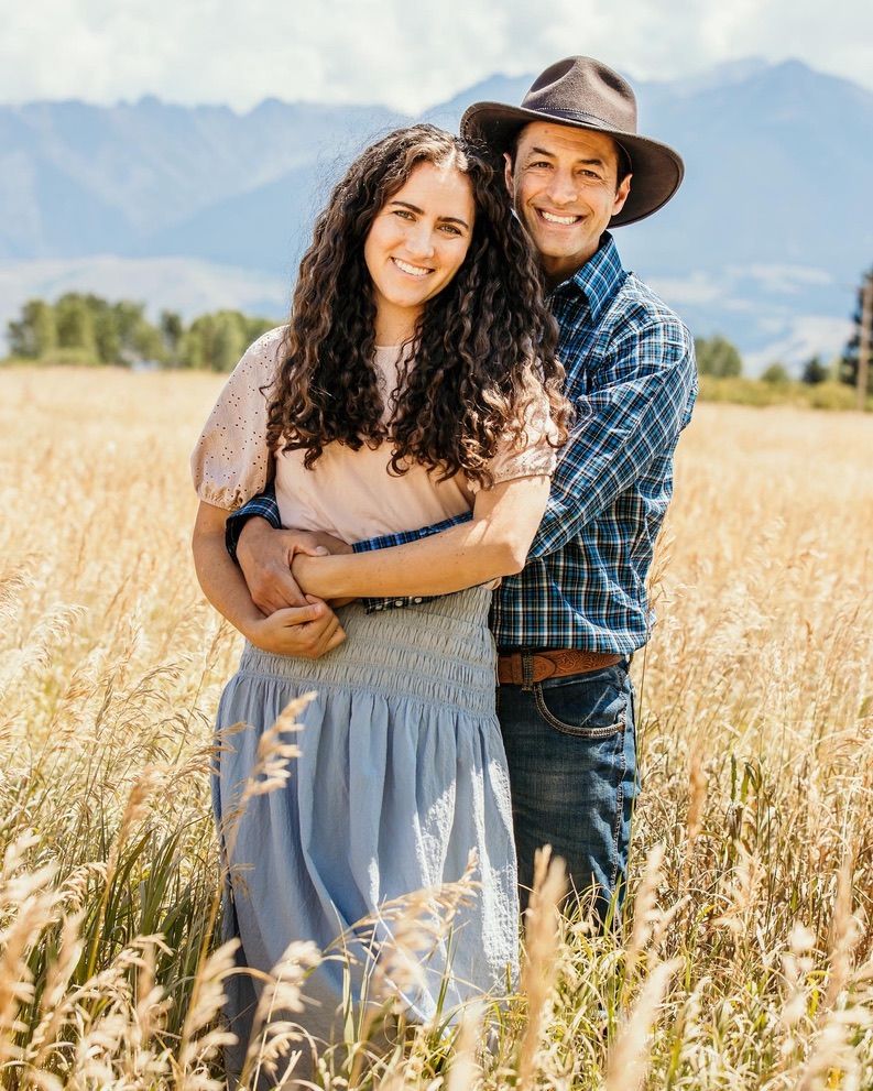 A couple embraces in a golden wheat field with mountain ranges in the distance.