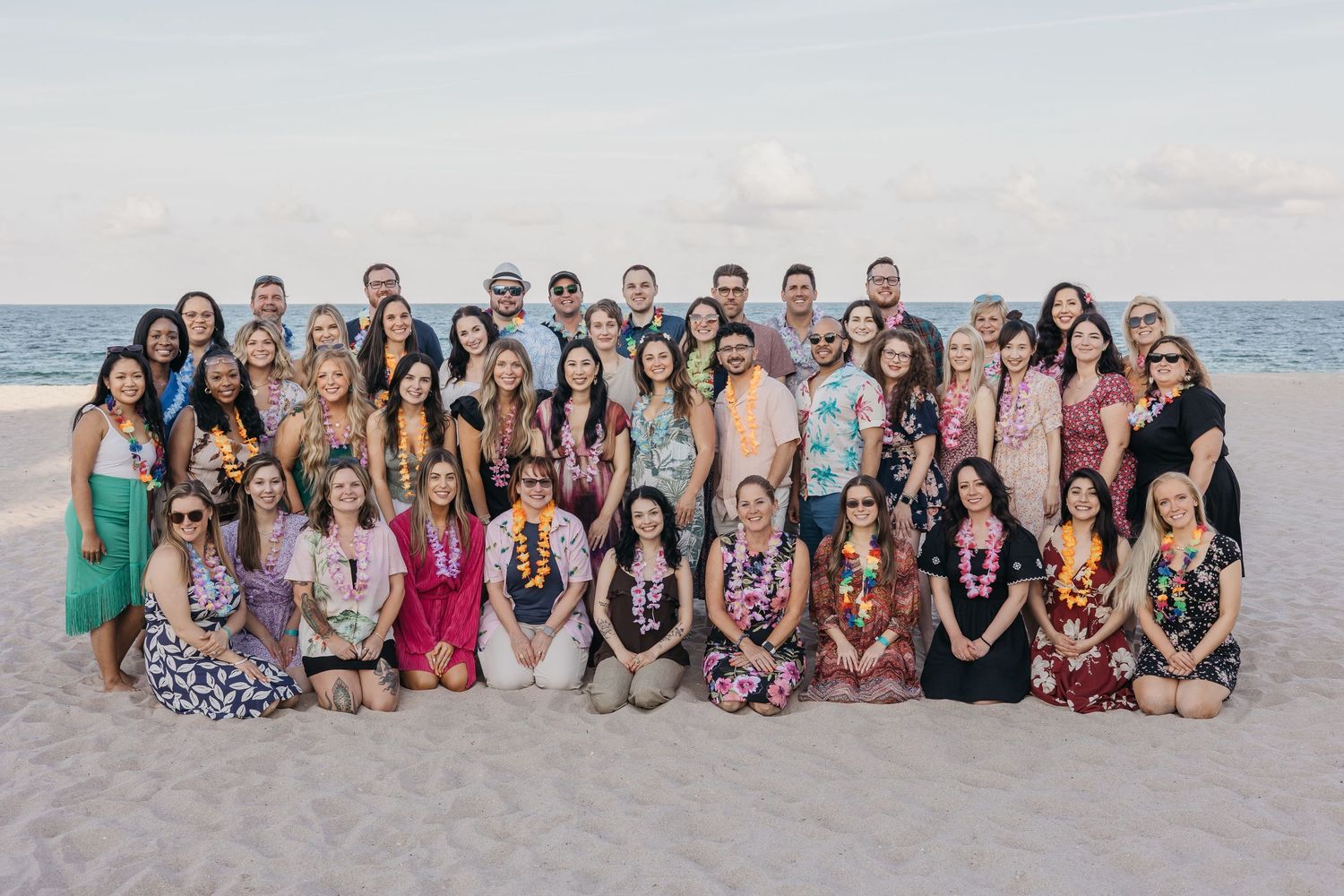 A large group of people gathered on a beach for a group photo at sunset.