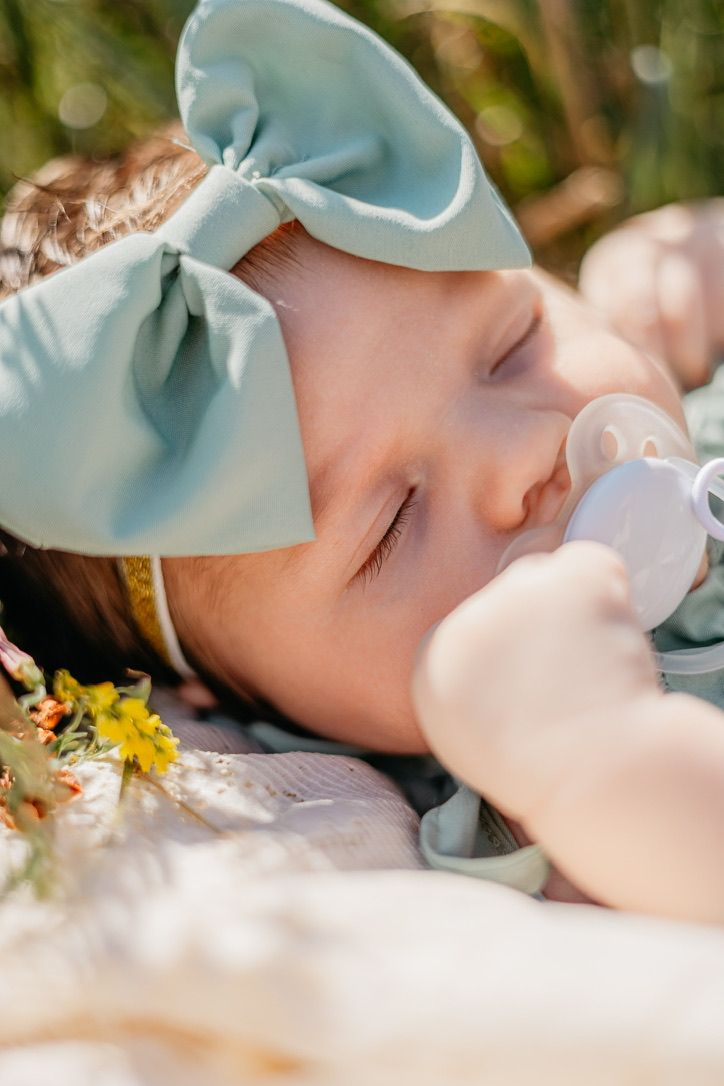 Close-up portrait of someone sleeping peacefully with a blue bow and flowers.