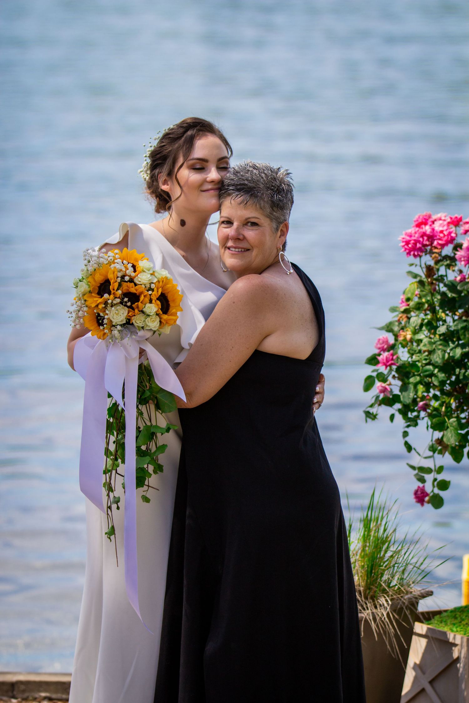 Intimate waterfront ceremony moment with black dresses and colorful floral arrangements.