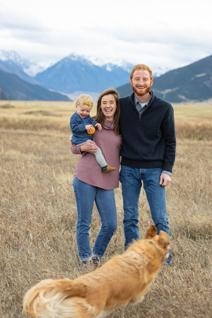 Family and golden retriever pose in field with mountain landscape behind them.