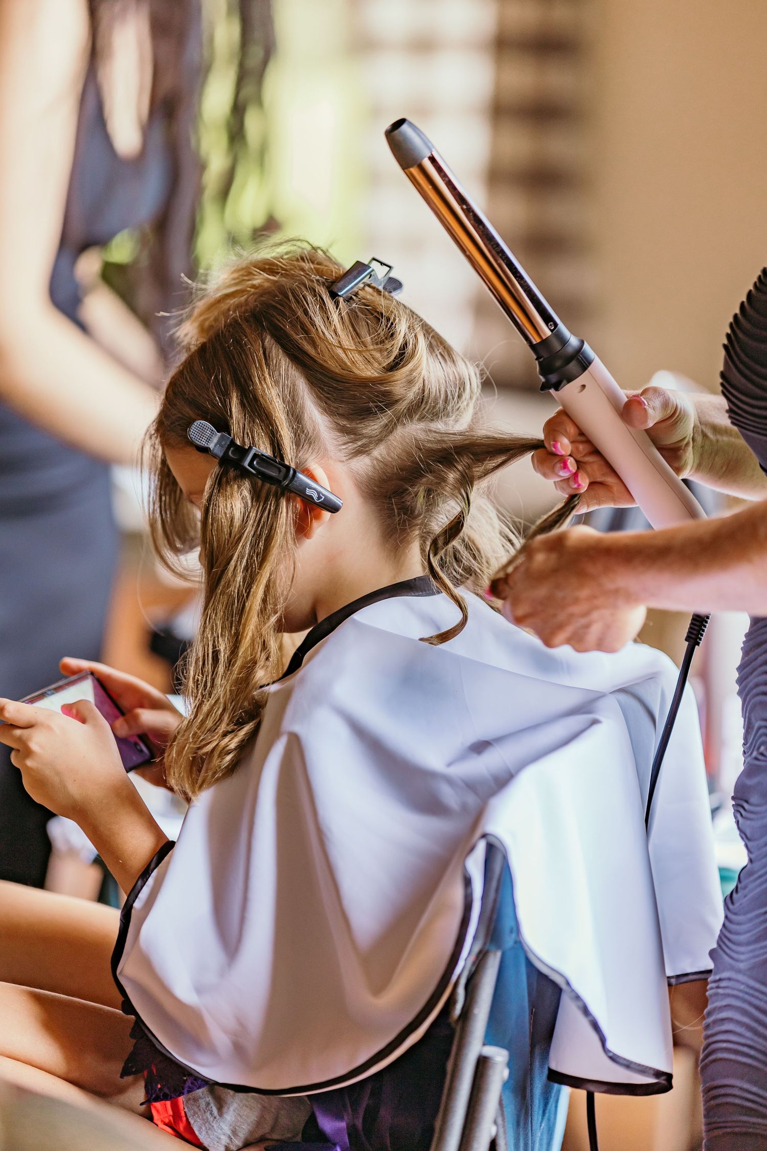 Hair styling session shows curling iron being used on light colored hair.