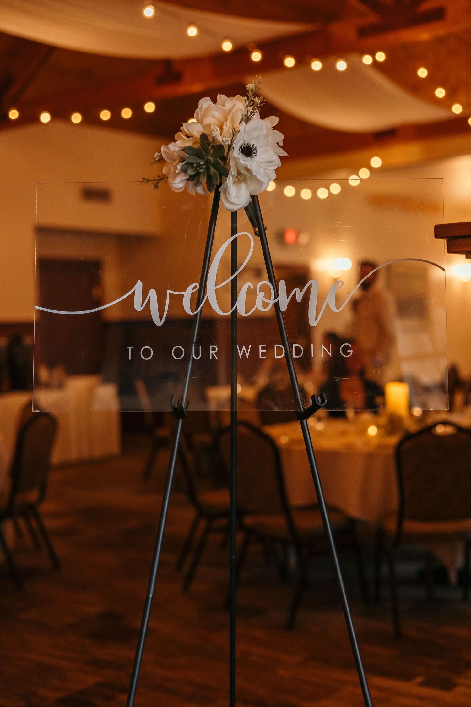 Wedding venue decorated with string lights and welcome sign in warm evening ambiance.