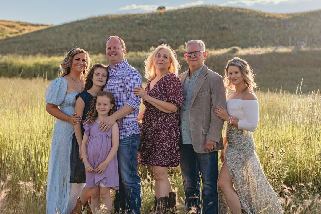 Extended family portrait in golden field with mountains at sunset.