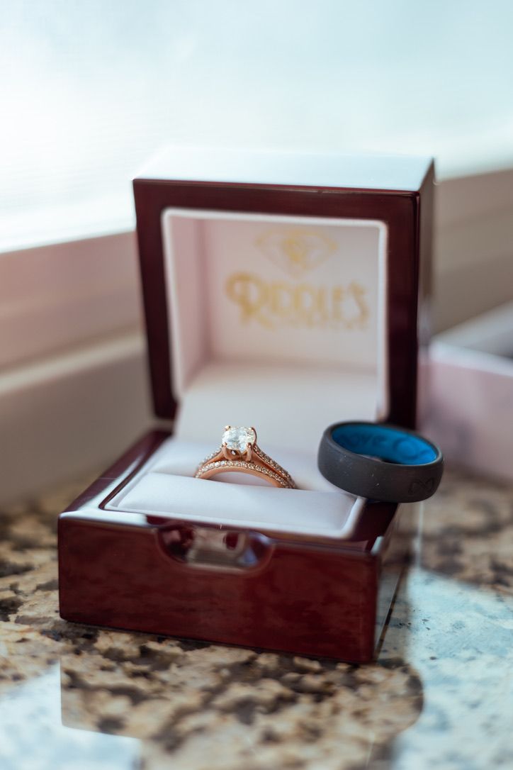 Wedding rings displayed in burgundy jewelry box on marble surface.