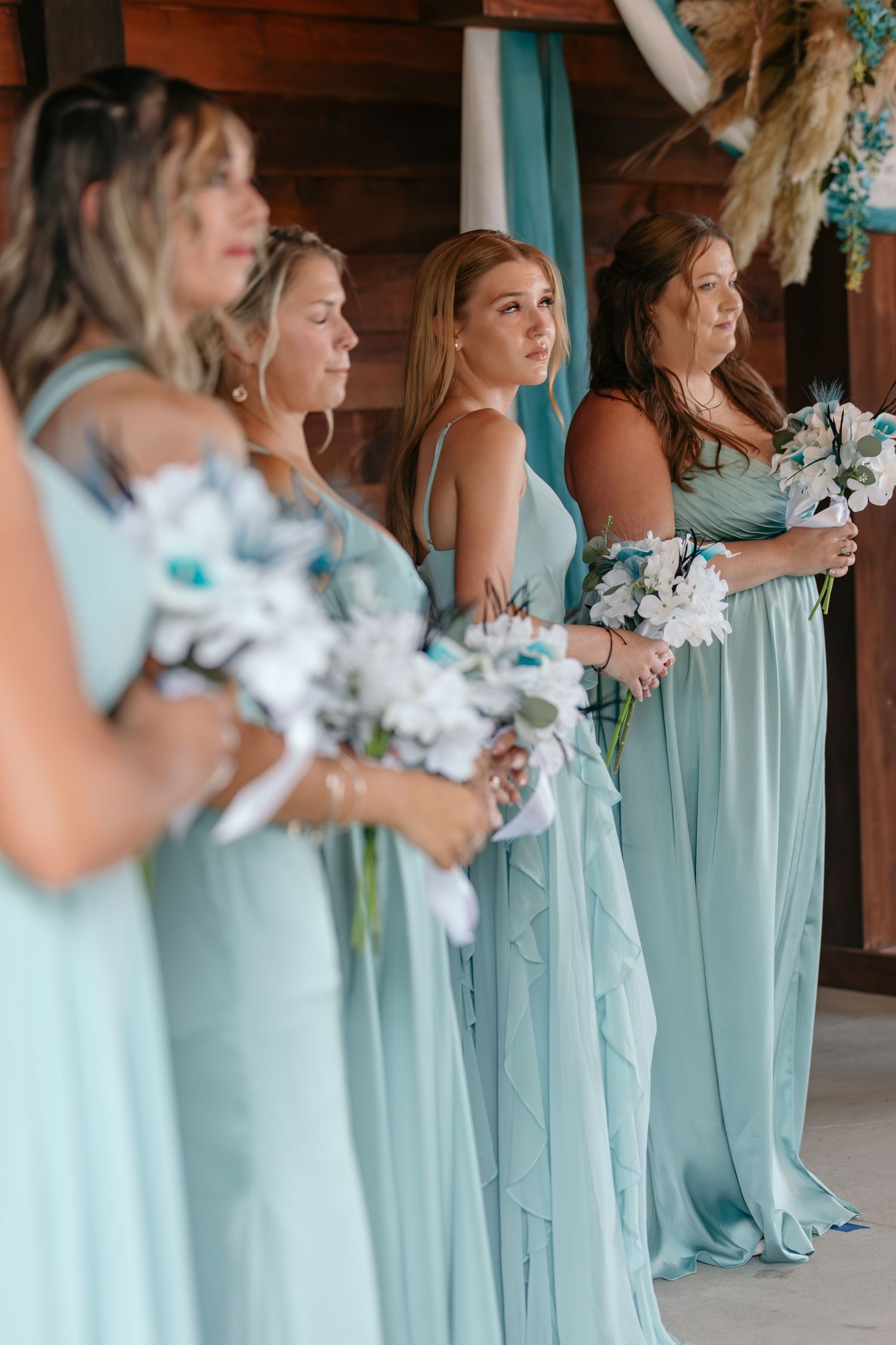 Row of bridesmaids in matching mint green dresses hold white bouquets during wedding ceremony.