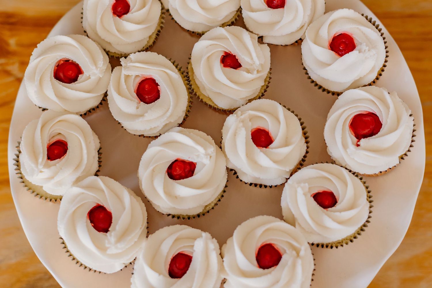 White frosted cupcakes topped with maraschino cherries arranged on serving plates.