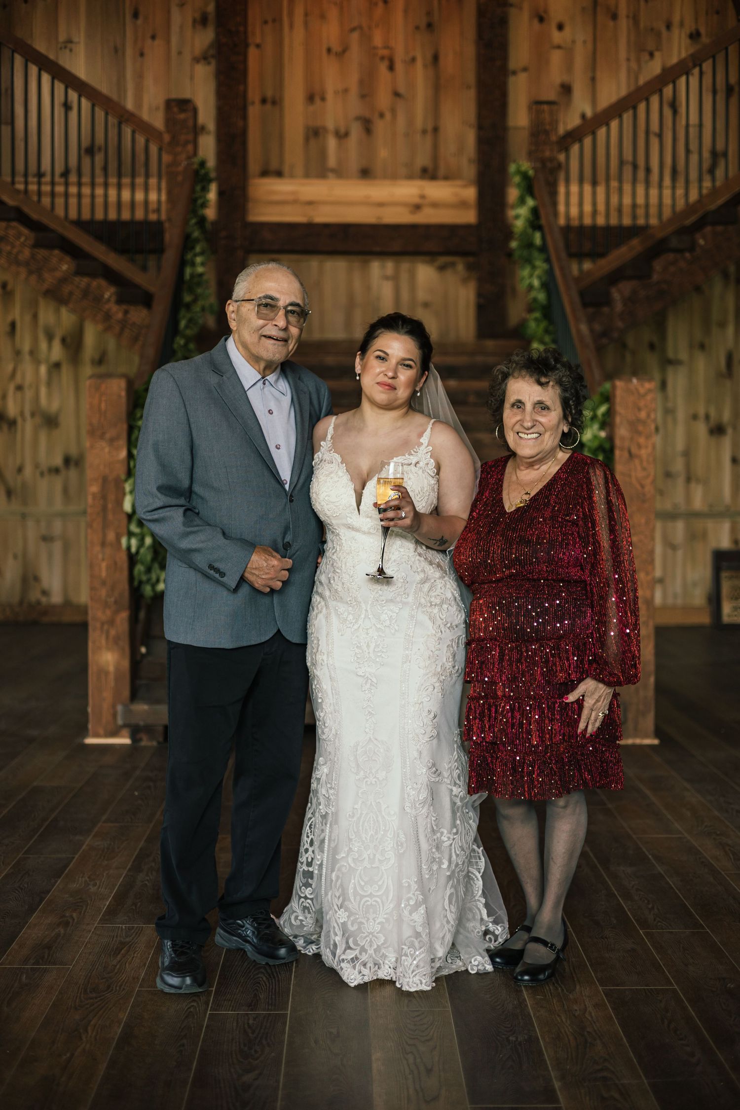 Three people pose together in formal attire inside a wooden barn venue.