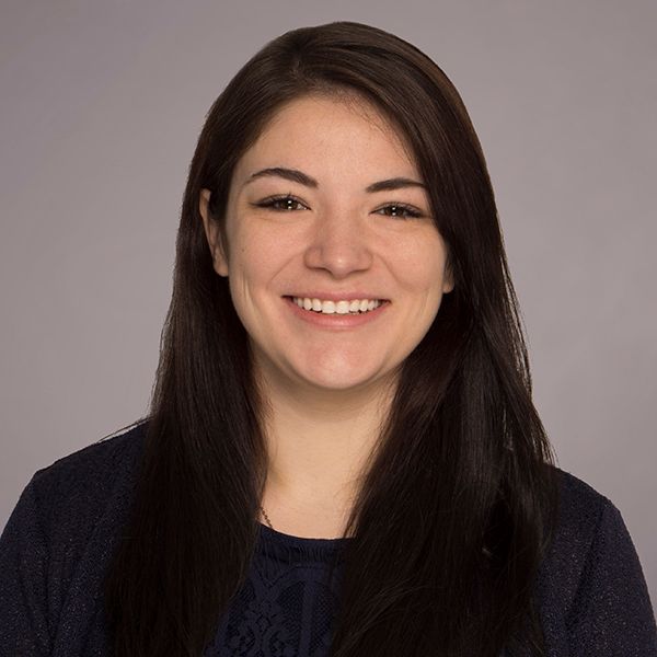 Professional headshot showing bright smile and dark hair against neutral backdrop.