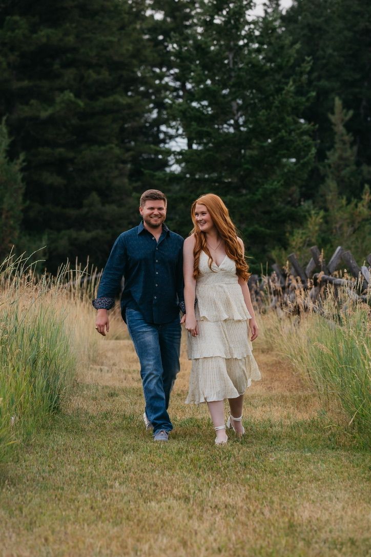 A couple walks hand in hand through tall grass in a natural outdoor setting.