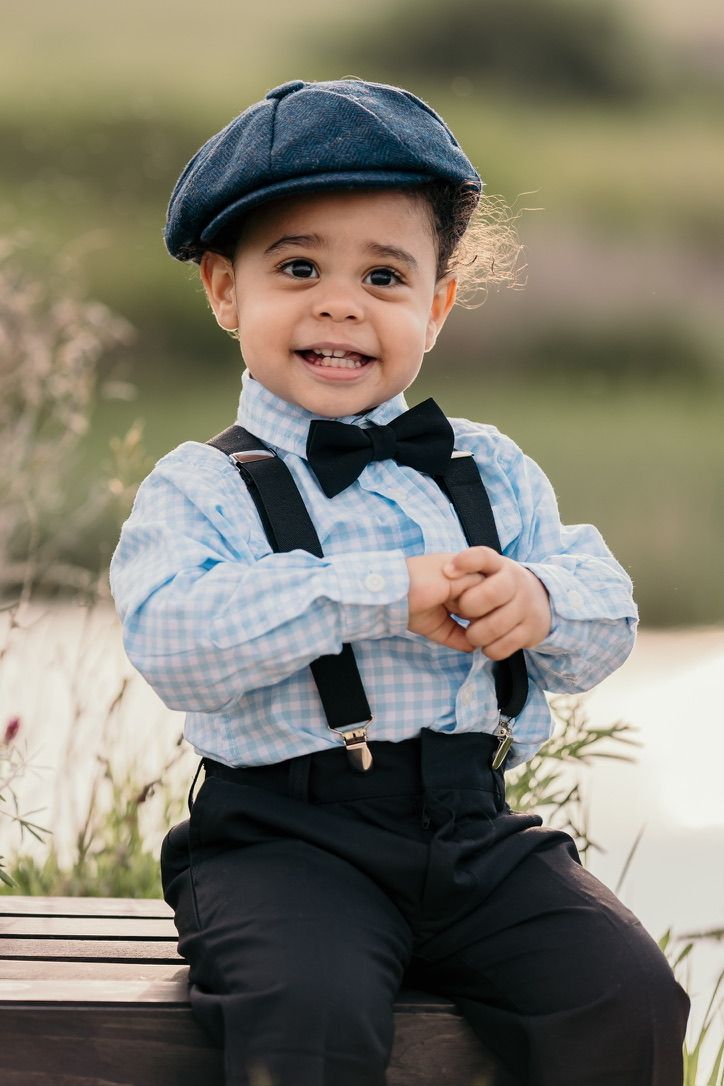 Child in vintage style outfit with suspenders and bow tie sitting outdoors.
