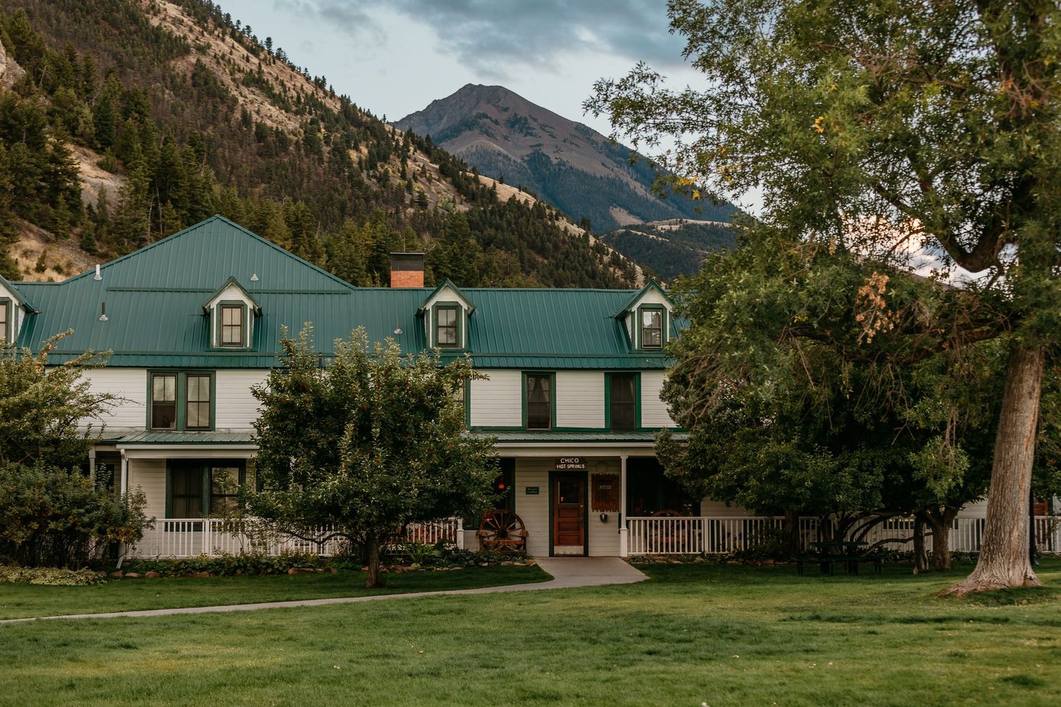 Mountain ranch venue with white farmhouse buildings and green lawn surrounded by scenic landscape.