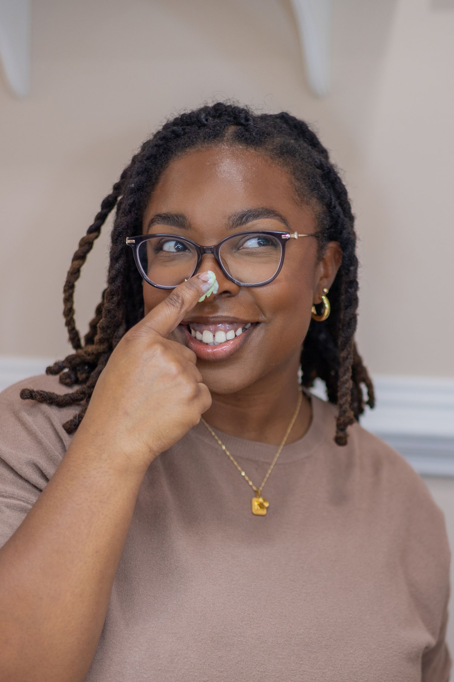 A person wearing glasses and a brown top poses with a cheerful expression.