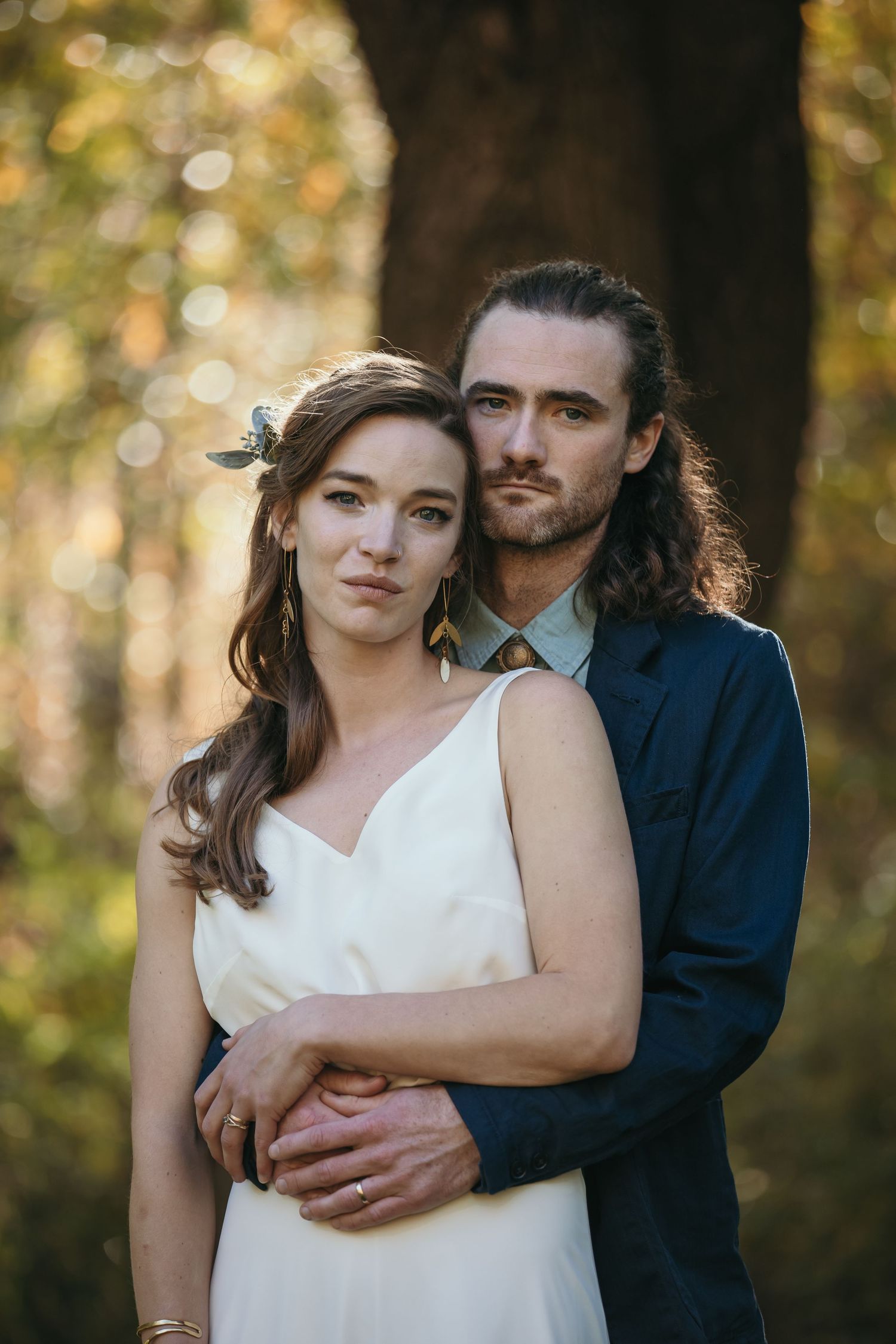 Romantic couple embraces in a forest setting with golden bokeh lighting in the background.