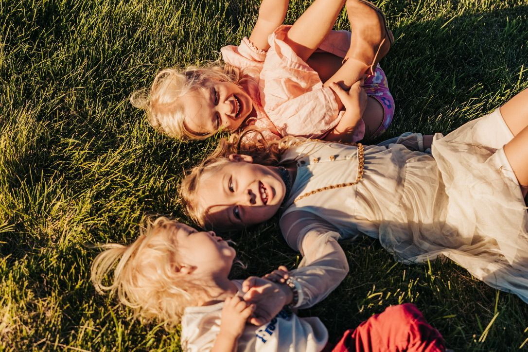 Three people lying in green grass during golden hour photography session.