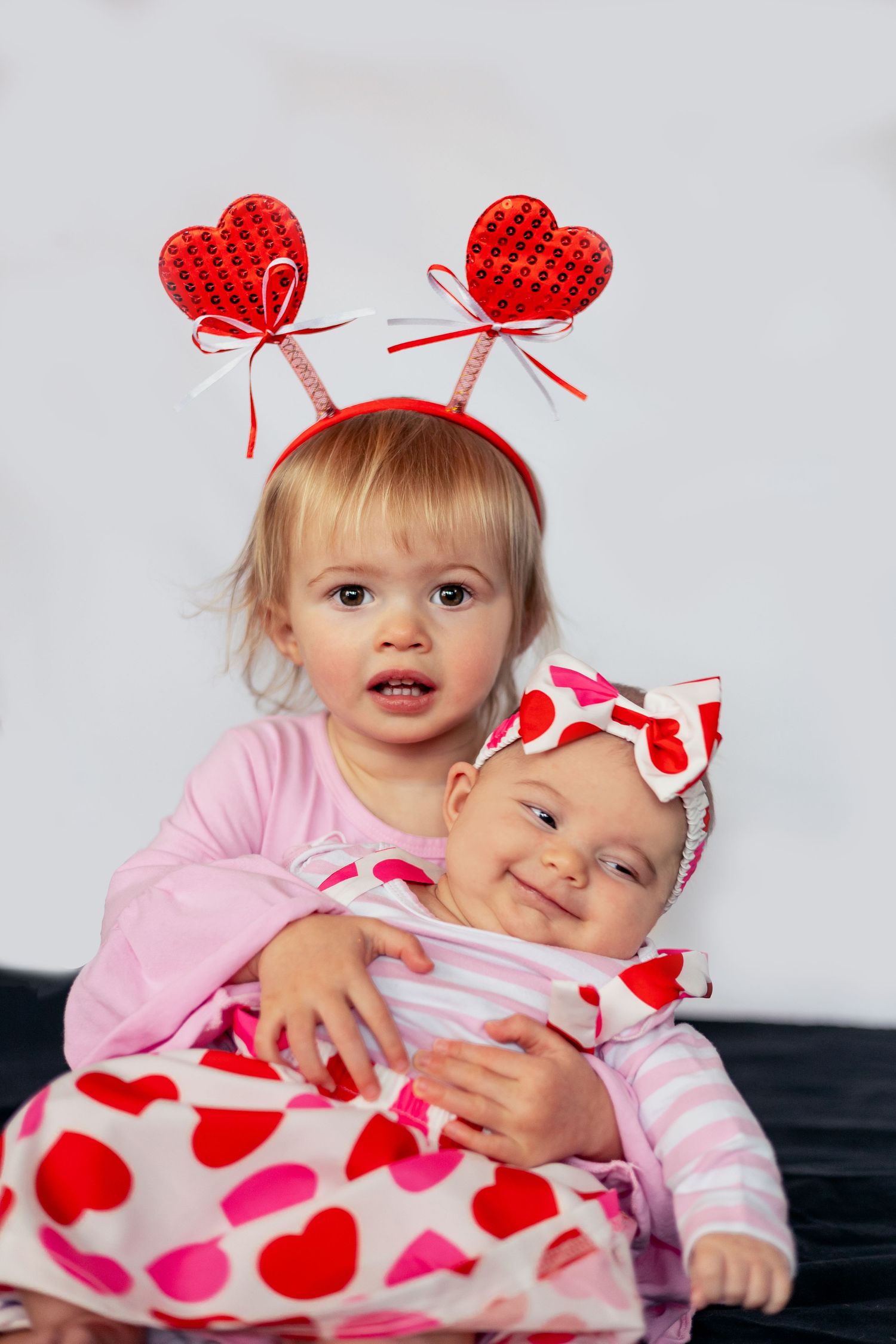 Two young children in Valentine's themed outfits with heart accessories pose together.