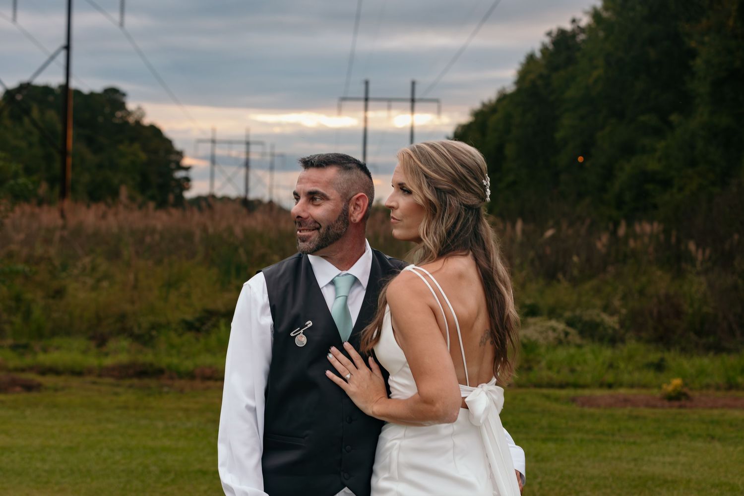 Romantic outdoor wedding photoshoot in a rustic field with power lines in background.