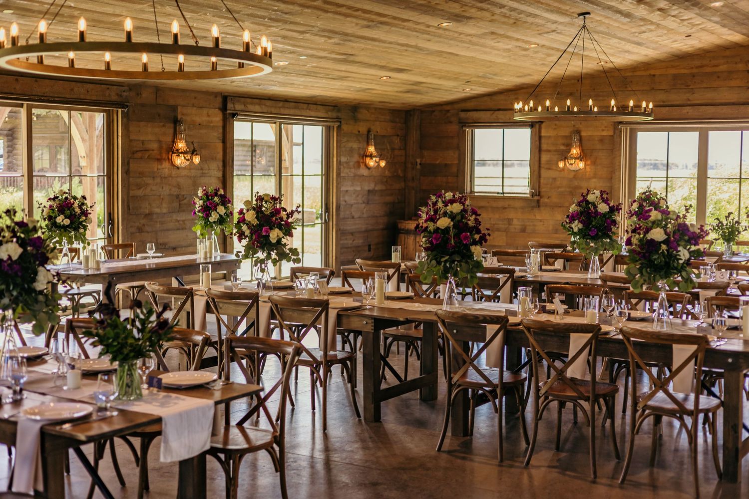 Rustic wooden reception venue with cross-back chairs and hanging string lights.