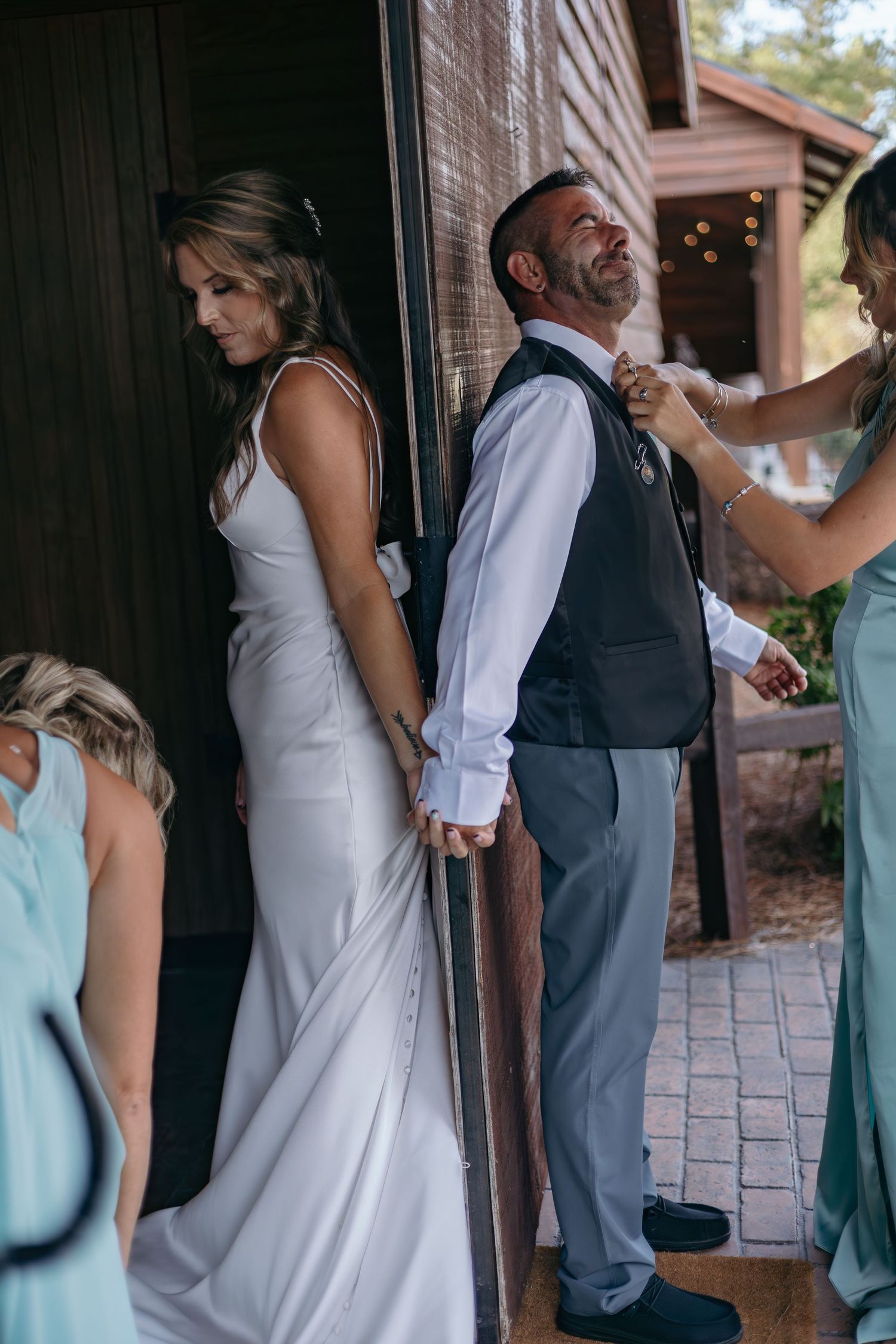 Wedding party members in formal attire gather outside a brick building during a first look moment.