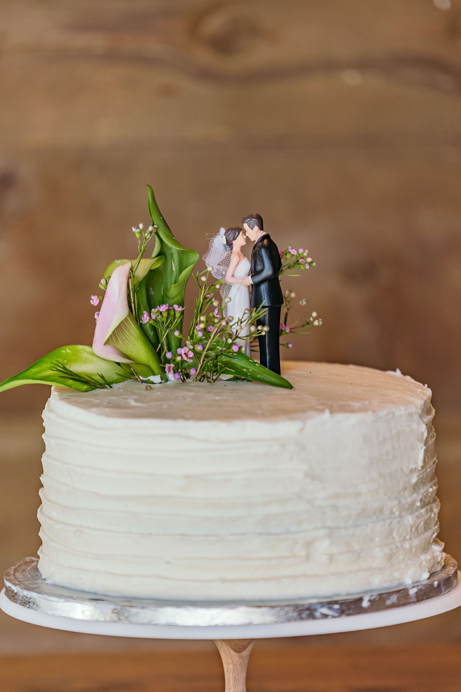 White wedding cake decorated with fresh flowers and a traditional cake topper on a silver stand.