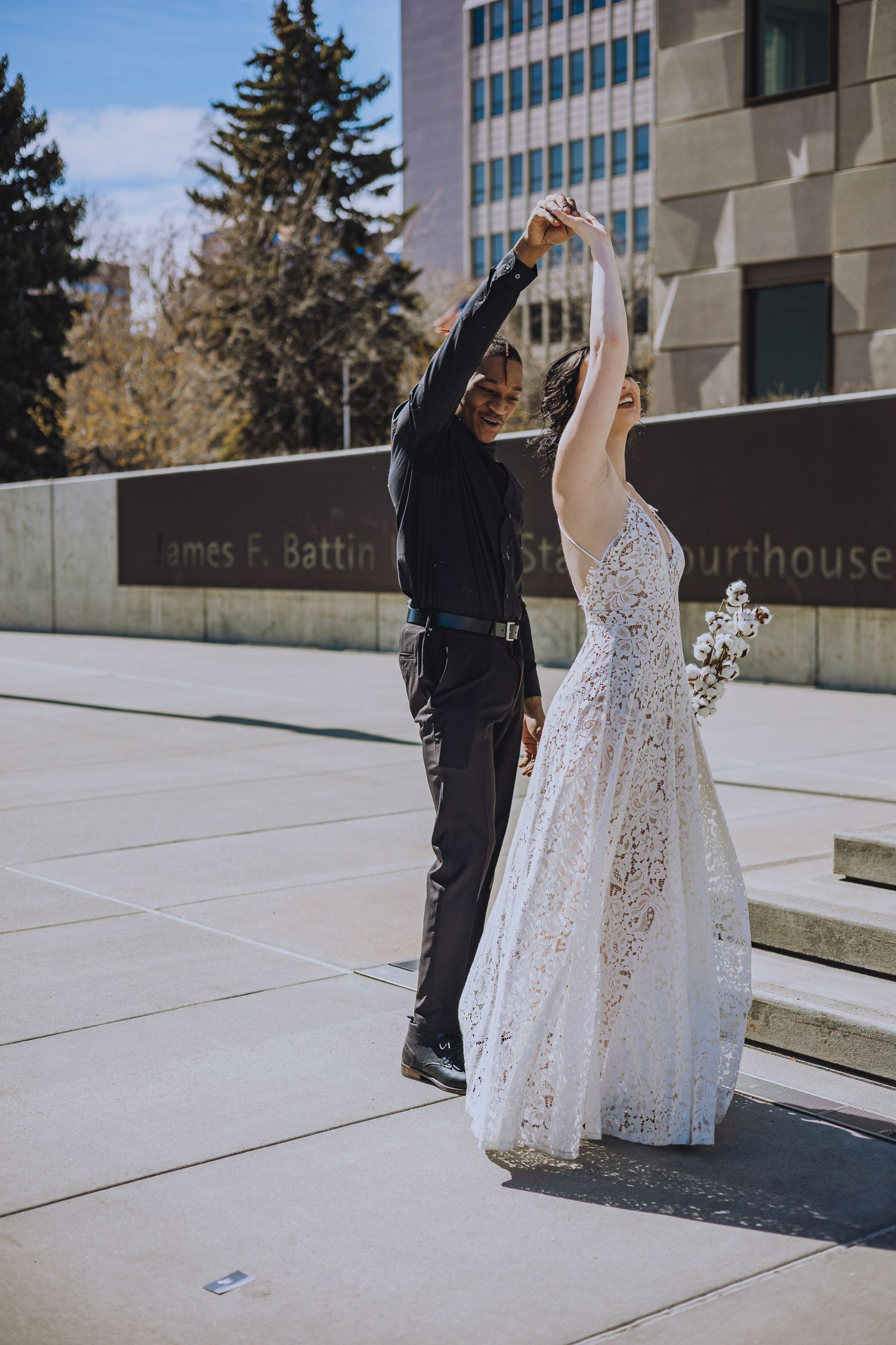 A couple dancing together on outdoor steps, with one wearing a sparkly white dress and the other in all black.
