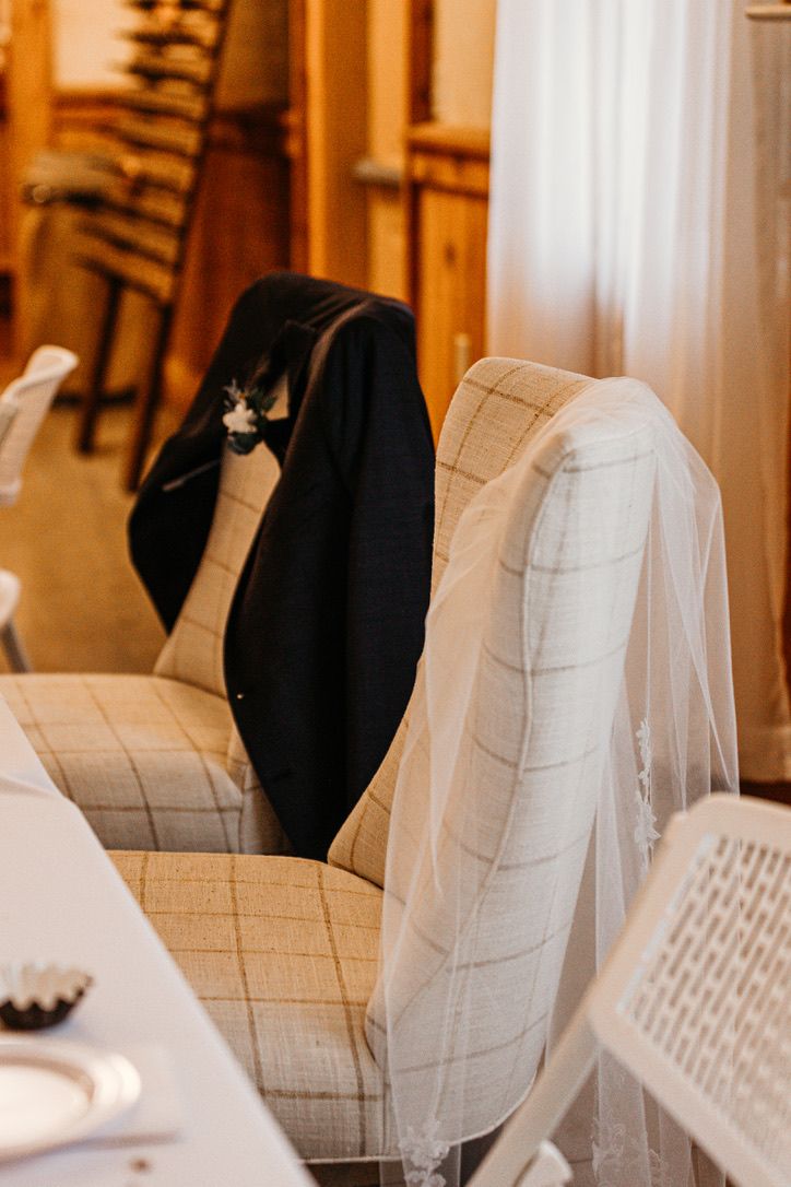 Wedding attire including black tuxedo jacket and white veil draped over upholstered chairs.