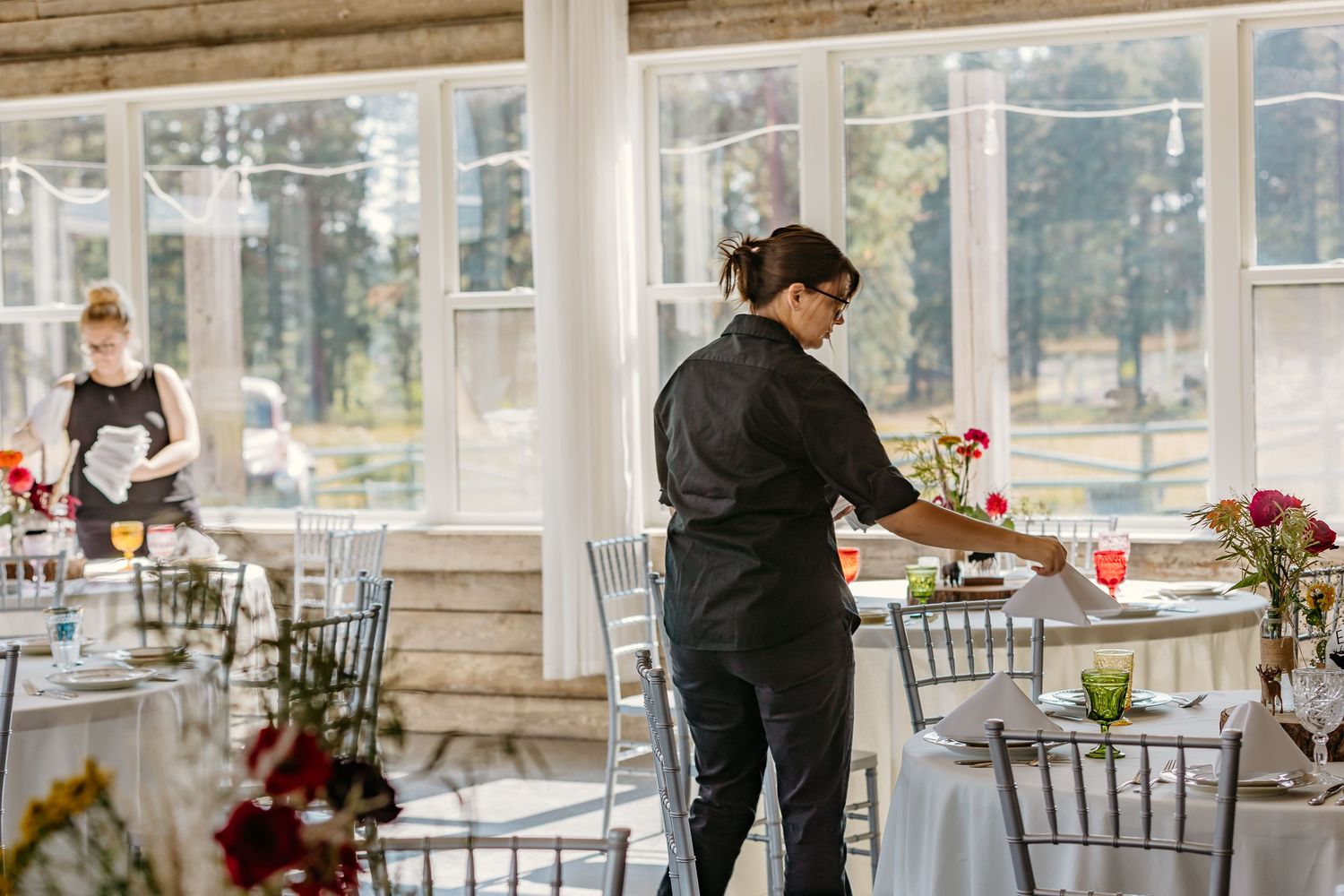 Staff preparing and setting up tables for an elegant indoor event with natural lighting.