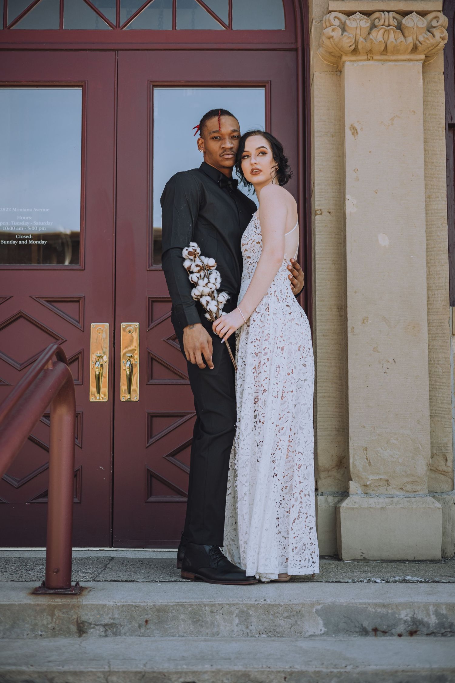 A couple poses together in front of ornate red doors during their wedding day.