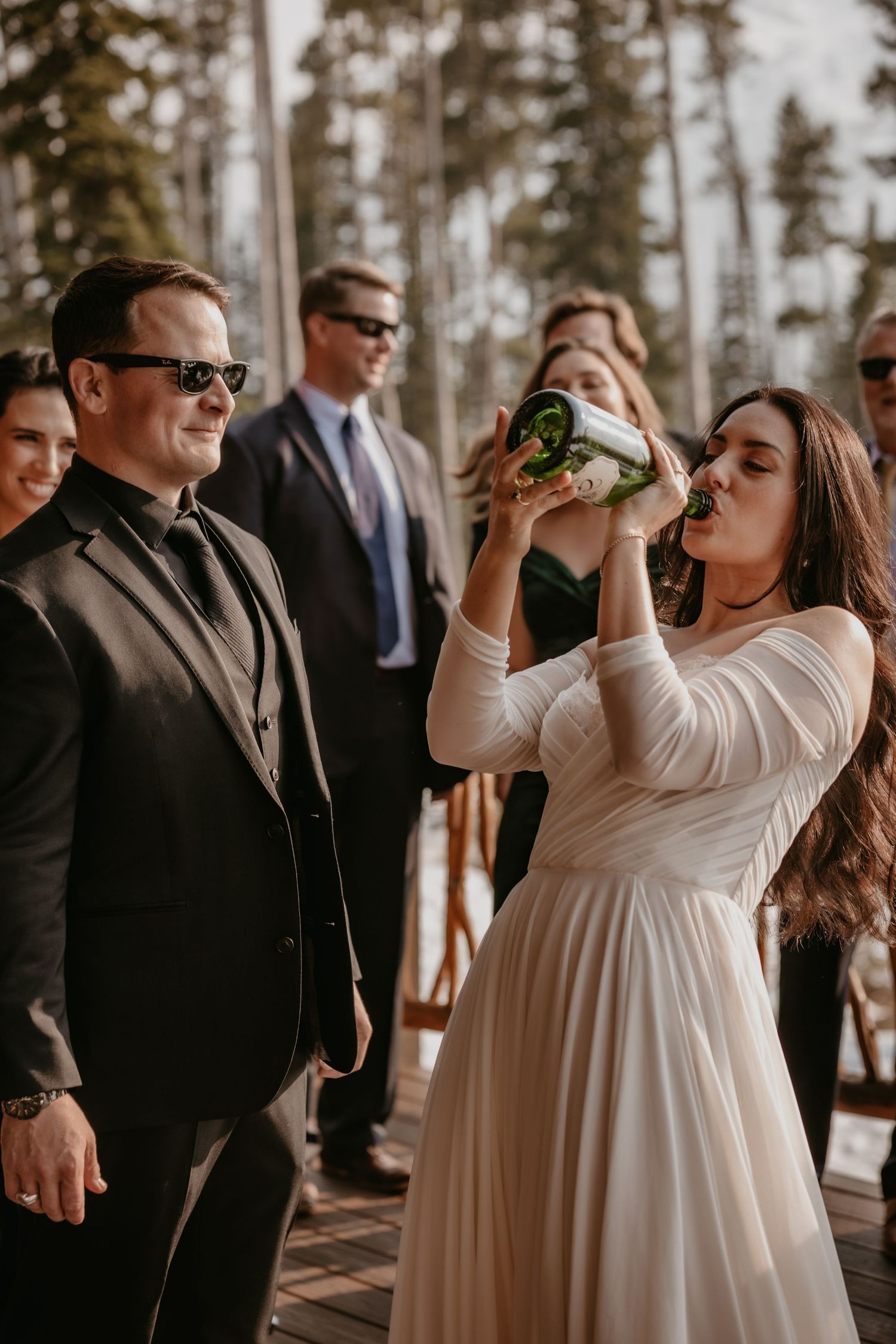 Wedding celebration in rustic outdoor venue with pine trees in background.
