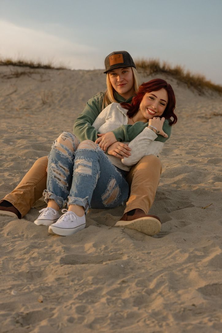 A couple relaxes together on sandy beach dunes at sunset.