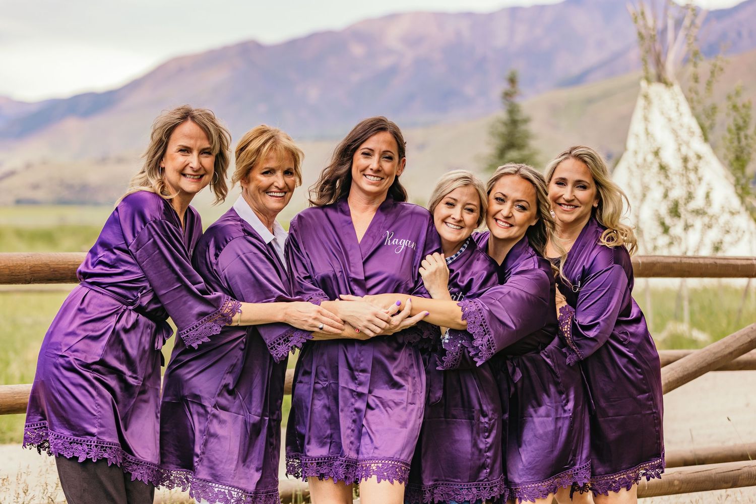 Bridesmaids in matching purple robes posing together outdoors with mountains in background.